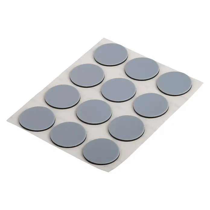 Suki Patín antideslizante para alfombras - Diámetro: 22 mm, Gris, 12 ud. - Imagen de un paquete de 12 deslizadores de muebles redondos grises sobre una hoja de soporte blanca, adecuados para su uso en diversas superficies.