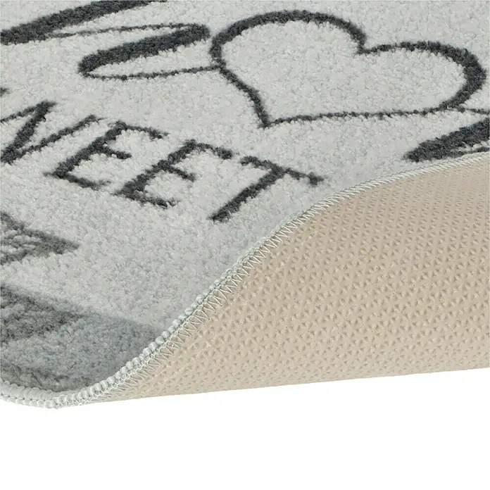 Fußmatte Home Sweet Home - Grau, 60 x 80 cm, 100 % Polyester - Nahaufnahme einer "Home Sweet Home"-Fußmatte mit Herzakzent, die ihre rutschfeste Unterseite und flauschige Textur zeigt.