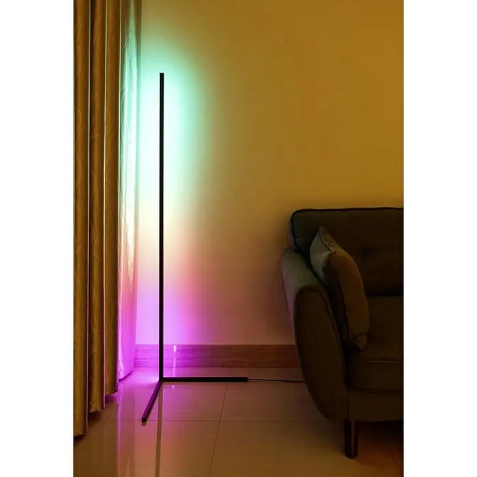 Tween Light LED-Stehleuchte Anzio - 19 W, Höhe: 140 cm, Schwarz, RGB - Ein schlanker, moderner Eck-LED-Bodenstrahler mit Farbwechsel beleuchtet stilvoll einen Wohnbereich neben Vorhängen und einem Sofa.