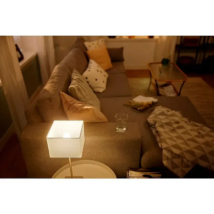 Philips Hue Smart-LED-Lampen Set White - E14, Dimmbar, Warmweiß, 470 lm, 5,5 W, Kerze, 1 Stk. - Nahaufnahme einer quadratischen Nachttischlampe mit warmem Licht, die eine gemütliche Atmosphäre in einem Wohnzimmer erzeugt.