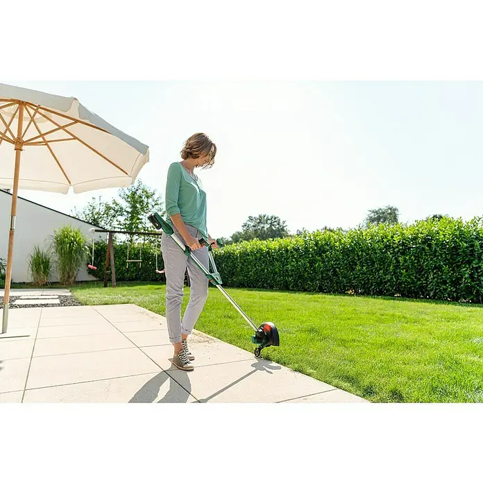 Bosch Power for All 18V Akku-Rasentrimmer UniversalGrassCut 18V-260 - 18 V, 2 Ah, 1 Akku - Eine Frau benutzt einen Bosch Rasentrimmer im Garten, um Rasenkanten zu schneiden. Der Rasentrimmer ist grün und schwarz.