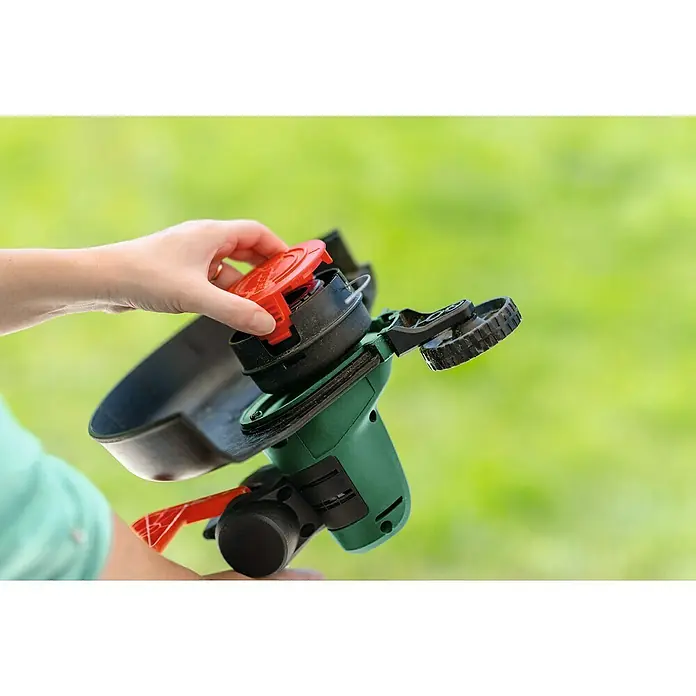Bosch Power for All 18V Akku-Rasentrimmer UniversalGrassCut 18V-26 - 18 V, Li-Ionen, Ohne Akku - Eine Hand setzt den roten Deckel auf einen grünen Rasentrimmer, der vor einem grünen Hintergrund gehalten wird.