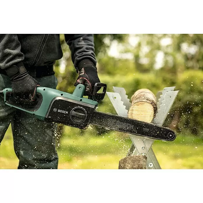 Bosch Elektro-Kettensäge UniversalChain 35 - 1.800 W, Schwertlänge: 35 cm - Person schneidet Holz mit einer grün-schwarzen Bosch Elektro-Kettensäge, Späne fliegen. Der Stamm liegt auf einem Sägebock.