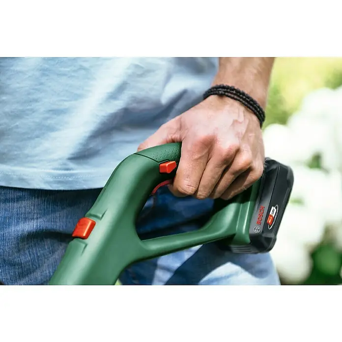 Bosch Power for All 18V Akku-Rasentrimmer EasyGrassCut 18V-230 - 18 V, 2 Ah, Li-Ionen, 1 Akku - Nahaufnahme einer Person, die einen grünen Bosch Akku-Trimmer hält, mit Fokus auf das Werkzeug und den Bediener in Aktion.