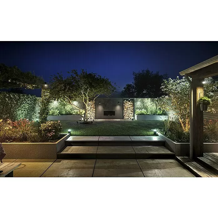 Philips Hue Verlängerungskabel - Schwarz, 2,5 m, IP67 - Ein moderner Garten bei Nacht, stimmungsvoll beleuchtet mit verschiedenen Außenleuchten, die Pflanzen, Bäume, eine Mauer und Terrassenstufen hervorheben.