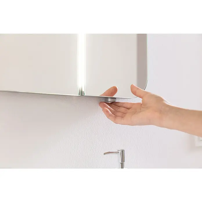 Camargue Lineo LED-Lichtspiegel - 70 x 85 cm - Eine Hand öffnet einen modernen Spiegelschrank mit integrierter Beleuchtung im Badezimmer, der Funktionalität und Design vereint.