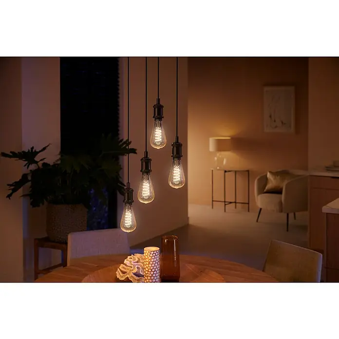 Philips Hue Smart-LED-Lampe White Ambiance Filament - E27, Dimmbar, Warmweiß, 550 lm, 7 W, Lampenbezeichnung: ST72, 1 Stk. - Moderne Pendelleuchten mit Edison-Glühbirnen beleuchten einen Esstisch mit dekorativen Elementen. Warmes, einladendes Licht sorgt für Ambiente.