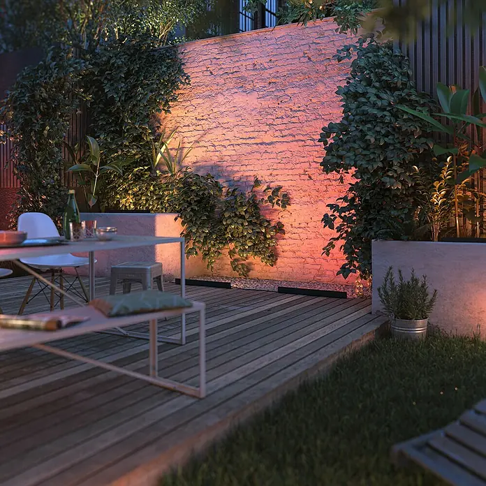 Philips Hue LED-Außenleuchte Amarant - Farbe Gehäuse: Schwarz, IP65, 20 W - Ein Gartentisch mit Stühlen und Bank auf einer Holzterrasse, umgeben von üppigem Grün und beleuchtet mit stimmungsvollem Licht.