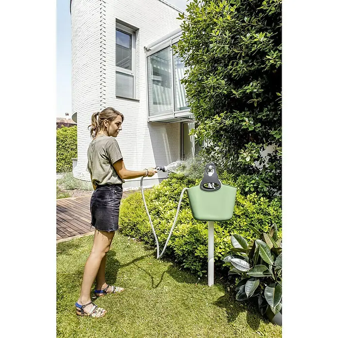 Gartenschlauch AquaGo Bunny - Schlauchlänge: 25 m, Grün - Eine Frau benutzt den Kärcher Wasserspender auf einer grünen Wiese mit einem modernen Haus im Hintergrund, um ihre Pflanzen zu gießen.