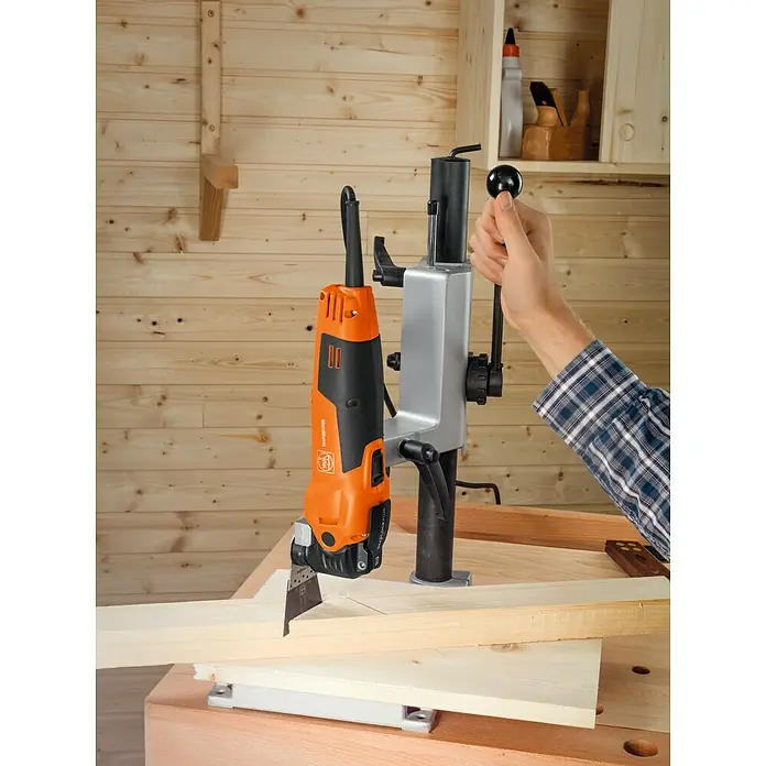 Fein Tisch- & Bohrständerhalterung - Passend für: Fein MultiMaster Multifunktionswerkzeuge - Das Bild zeigt eine oszillierende Multimaster-Säge von Fein mit Führung am Werkstück, bedient von einer Hand, im Holzhintergrund.