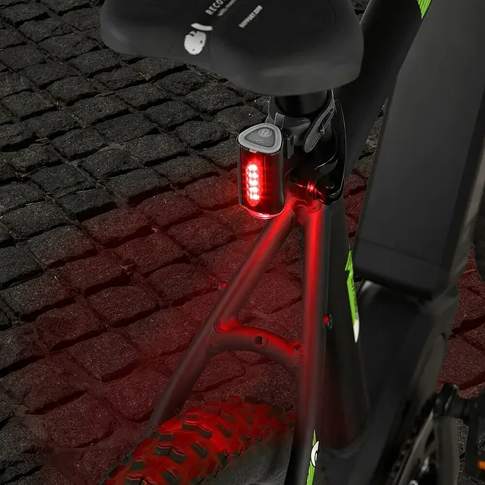 Fischer LED-Akkuleuchten-Set Twin - 5 -tlg., Beleuchtungsstärke: 50 lx, Leuchtdauer: 4 h, Spritzwassergeschützt - Nahaufnahme eines Fahrradrücklichts, das an einem schwarzen Fahrradrahmen befestigt ist und rotes Licht ausstrahlt.
