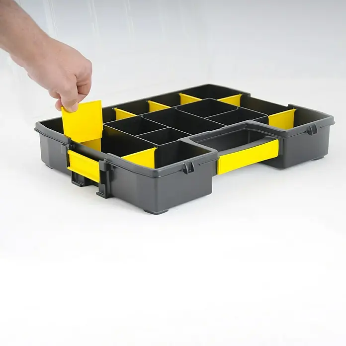 Stanley Kleinteilekoffer Sortmaster Junior - L x B x H: 29,2 x 37,5 x 6,7 cm - Graue Werkzeugkiste mit gelben Trennwänden, bei der eine Trennwand von einer Hand eingesetzt wird. Ideal zur Organisation von Kleinteilen.