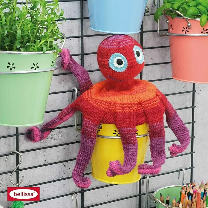 Bellissa Wandboard Fermo60,5 x 99 cm, Stahl - Ein handgestrickter, roter Oktopus mit acht Armen hängt an einem gelben Eimer an einer Wandgitterstruktur.