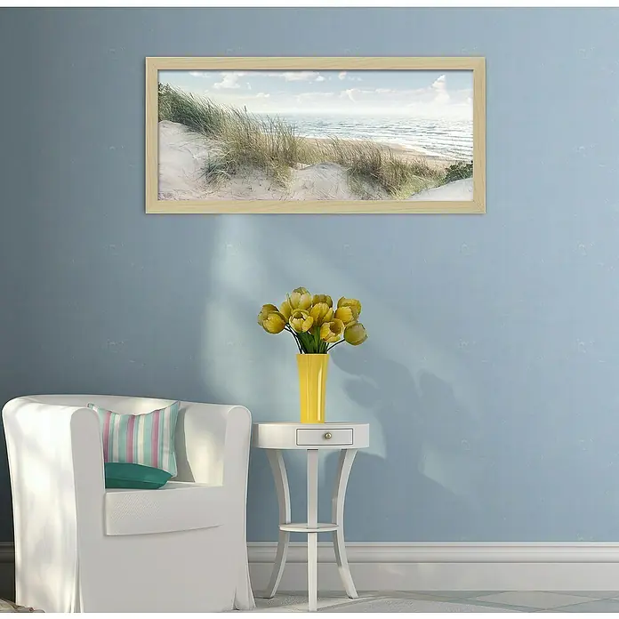 ProArt Bild Oversized - Baltic Sea Coast, B x H: 124 x 50 cm - Ein Küstenlandschafts-Kunstdruck in einem hellen Holzrahmen schmückt die Wand über einem Arrangement mit einer Vase und Möbeln.