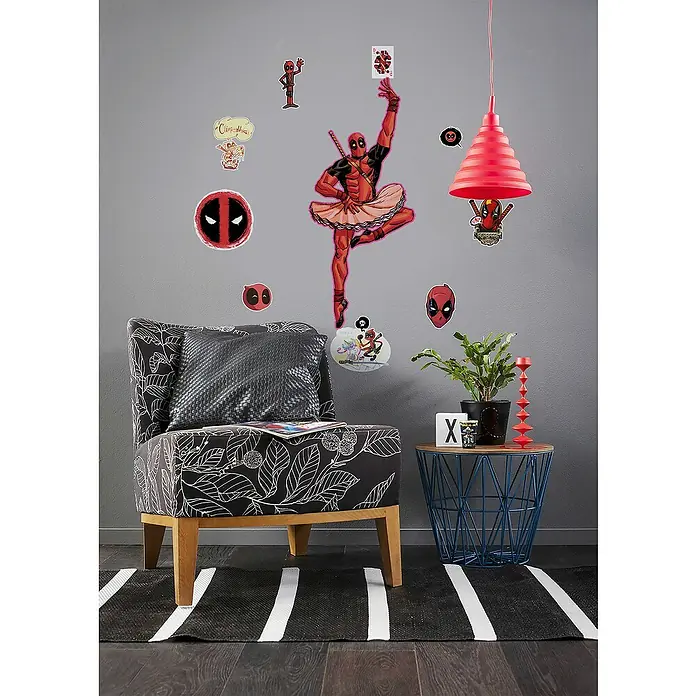 Komar Marvel Wandtattoo Deadpool Derppool - Schwarz, Rot, 50 x 70 cm, 10 -tlg. - Ein stilvoller Sessel mit Blattmuster und glänzendem Kissen vor einer grauen Wand mit Deadpool-Dekorationen.