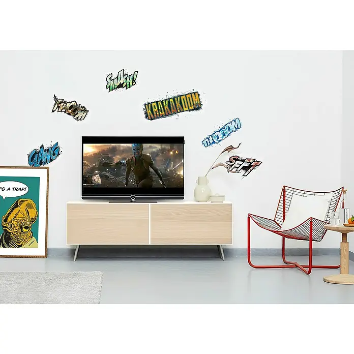 Komar Marvel Wandtattoo Avengers Sounds - Bunt, 50 x 70 cm, 6 -tlg. - Wanddeko mit Comic-Sprechblasen neben einem TV-Gerät und einem roten Stuhl. Die Wandsticker verleihen dem Raum einen dynamischen, pop-artigen Touch.
