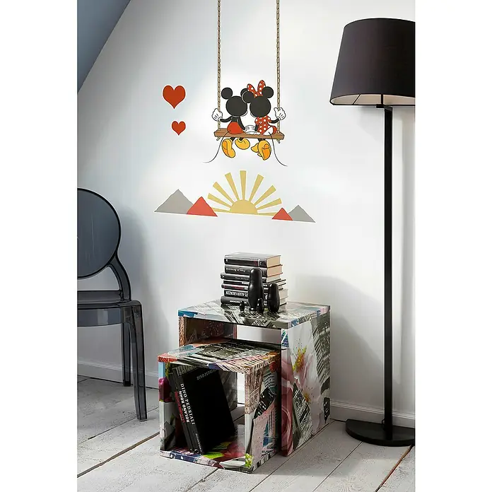 Komar Wandtattoo Mickey Mouse Swing - Bunt, 50 x 70 cm, 7 -tlg. - Blick auf zwei bunten Satztische mit Bücherstapel und Matroschkas, dekoriert mit Mickey Mouse Wandaufkleber und einer Stehlampe.