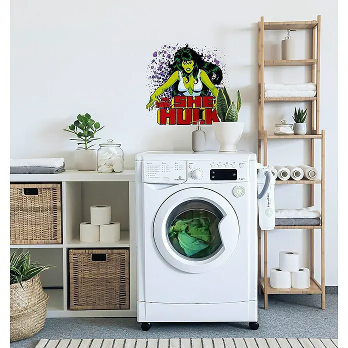 Komar Marvel Wandtattoo She Hulk - Grün, Gelb, 50 x 70 cm, 1 -tlg. - Waschmaschine mit She-Hulk Wandaufkleber im Waschraum. Die Maschine ist weiß und im Waschraum stehen Regale und Pflanzen zur Dekoration.
