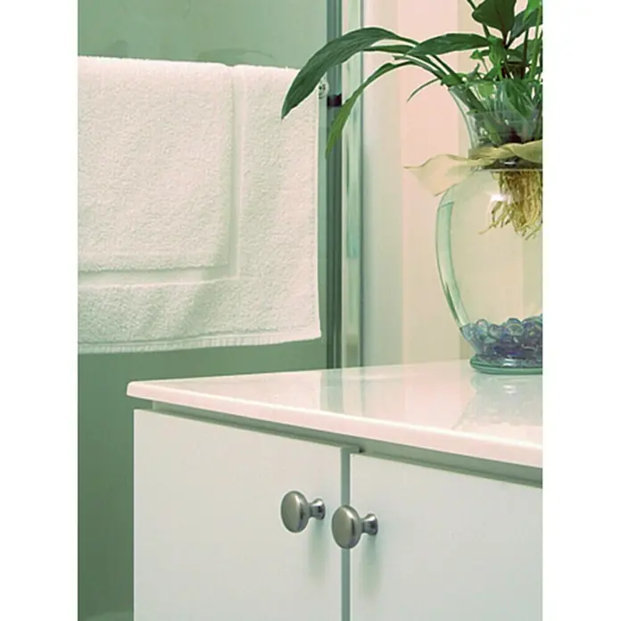 Rei Pomo para muebles 760 - Diámetro: 25 mm, Cromado, Cromo - Vista detallada de un mueble de baño con puertas blancas y pomos plateados, junto a una toalla y una planta en vidrio.