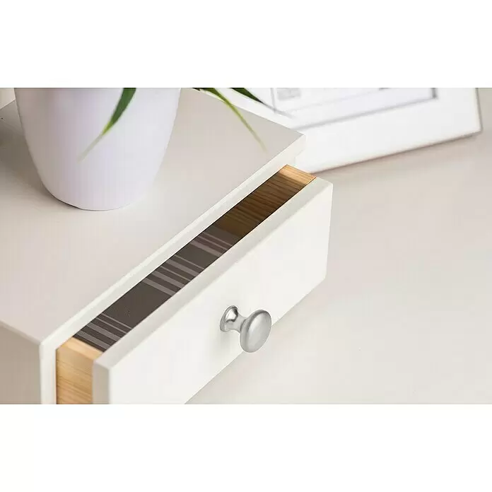 Rei Pomo para muebles 760 - Diámetro: 25 mm, Cromado, Cromo - Cajón blanco con pomo plateado, ligeramente abierto mostrando un interior a rayas. Una maceta encima y un marco de fotos al fondo.