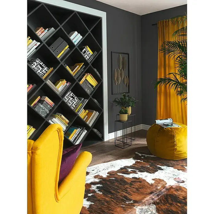 Esbeco Alfombra de piel de vaca - Exótico oscuro, 100% piel auténtica - Acogedora sala de estar con una estantería inclinada, un sillón amarillo y un puf a juego.