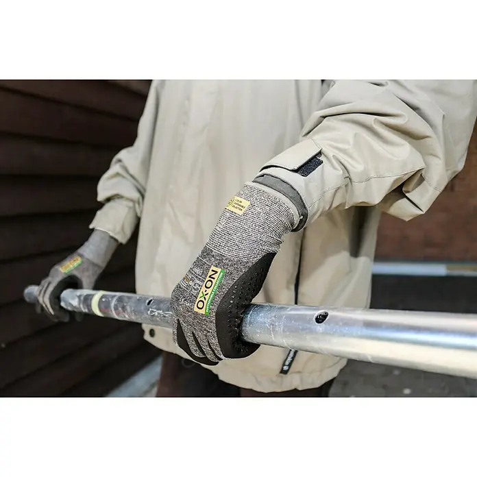 OX-ON Arbeitshandschuhe Recycle Supreme 16603 - Grau/Schwarz, 11 - Bild eines Mannes mit OX-ON Montagehandschuhen, der ein Metallrohr hält. Die Handschuhe bieten guten Grip und Schutz.