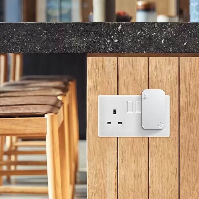 Ring Alarm Signalverstärker 2. Gen. - Weiß, 2,3 x 4,6 x 8 cm, Reichweite ca.: 76 m - Weißer Ring Chime Pro in einer britischen Steckdose an einer Holzkücheninsel. Das Gerät ist kompakt und fügt sich gut in die Umgebung ein.