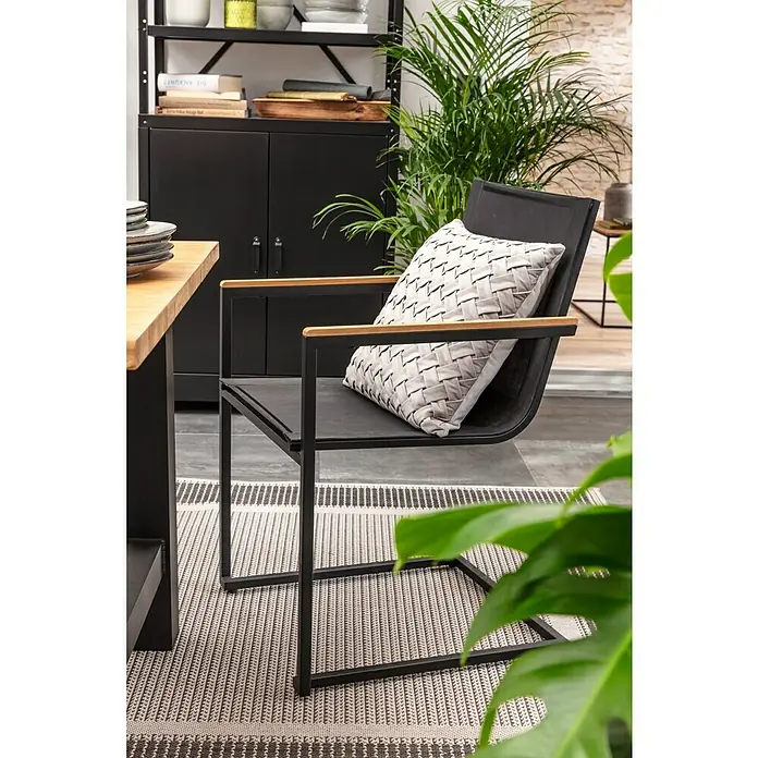 SENSUM Gartenstuhl Skuru - Edelstahl, Schwarz, B x T x H: 58 x 55 x 86 cm - Moderner schwarzer Stuhl mit Holzarmlehnen und gemustertem Kissen auf einem gestreiften Teppich.
