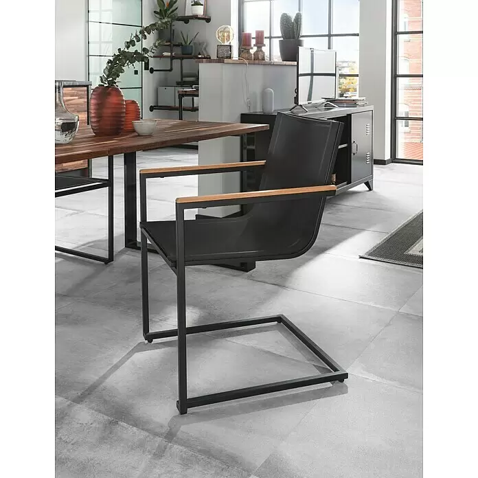 SENSUM Gartenstuhl Skuru - Edelstahl, Schwarz, B x T x H: 58 x 55 x 86 cm - Schwarzer Sessel mit Holzarmlehnen, Metallrahmen und Netzgewebe, neben einem Holztisch in einem modernen Raum.