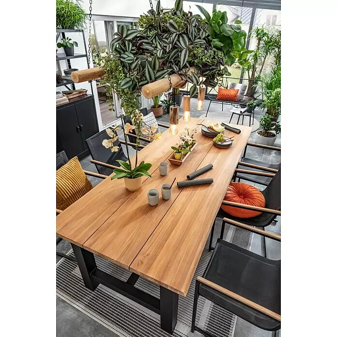 Sunfun Gartentisch - L x B x H: 240 x 100 x 75 cm, Aluminium. Teak, Rechteckig, Natur/Anthrazit - Großer Esstisch aus Holz mit schwarzem Metallgestell, gedeckt in einem hellen, pflanzenreichen Wintergarten.