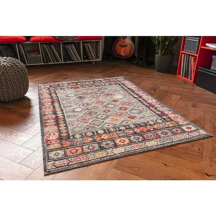 Outdoor-Teppich Bonnie - Bunt Hell, 170 x 120 cm, 100 % Polypropylen - Ein detailreicher Teppich mit geometrischen Mustern und warmen Farben liegt auf einem Holzboden in einem stilvollen Wohnraum.