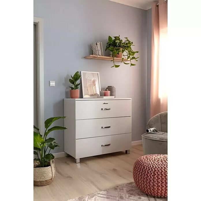 SCHÖNER WOHNEN-Farbe Wandfarbe Designfarbe - Klares Eisblau, Matt, 2,5 l, Konservierungsmittelfrei - Weiße Kommode mit drei Schubladen und silbernen Griffen und Füßen, dekoriert mit Pflanzen und Kerzen in einem Wohnraum.