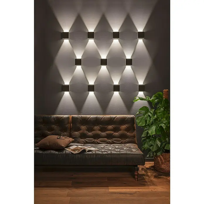 Starlux LED-Außenwandleuchte Umea - 8 W, 10 x 10 x 10 cm, Anthrazit, IP54 - Wandleuchten erhellen stilvoll den Raum über einem Ledersofa mit Kissen und Zeitschrift, neben einer Zimmerpflanze im Korb.