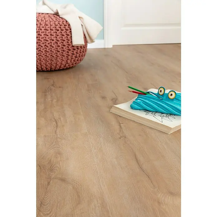 b!design Vinylboden Rigid Maxi - Ashton Eiche, Landhausdiele, 1.220 x 228 x 4,8 mm - Ein helles, holzartiges Laminat mit einem Notizblock, Stiften und einem krokodilförmigen Federmäppchen. Im Hintergrund ist ein rosa Pouf zu sehen.