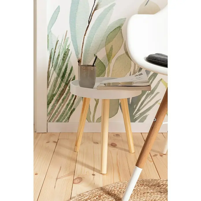 Komar Fototapete Breeze - 7 -tlg., B x H: 350 x 250 cm, Vlies - Nahaufnahme eines weißen Beistelltisches mit hölzernen Beinen, auf dem eine Tasse und ein Buch stehen, vor einer Wand mit Pflanzenmuster.