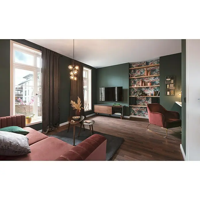 SCHÖNER WOHNEN-Farbe Wandfarbe DesignfarbeBesinnliches Waldgrün, Matt, 1 l, Konservierungsmittelfrei - Ein gemütliches Wohnzimmer mit einem modernen Sofa, einem stilvollen Sessel und einem eleganten TV-Möbel. Die dunklen Wände schaffen eine behagliche Atmosphäre.