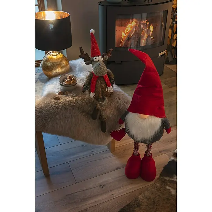 Tween Light Tischleuchte Gala - 40 W, Schwarz/Gold, G9 - Festliches Stillleben mit Weihnachtsdekorationen, darunter ein Elch, ein Gnom und ein Kaminfeuer, die eine warme, weihnachtliche Atmosphäre schaffen.