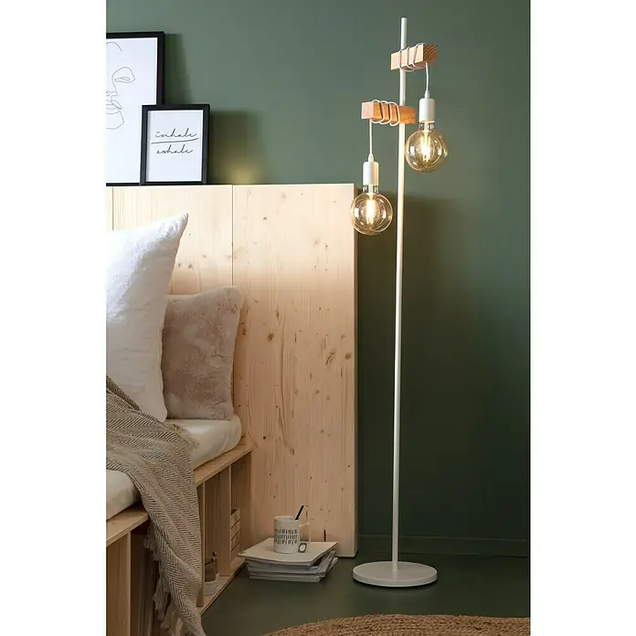 SCHÖNER WOHNEN-Farbe Wandfarbe Designfarbe - Ausgeglichenes Piniengrün, Matt, 2,5 l, Konservierungsmittelfrei - Eine moderne Stehlampe mit zwei Edison-Glühbirnen und Holzdetails neben einem stilvollen Bett mit Holzkopfteil.