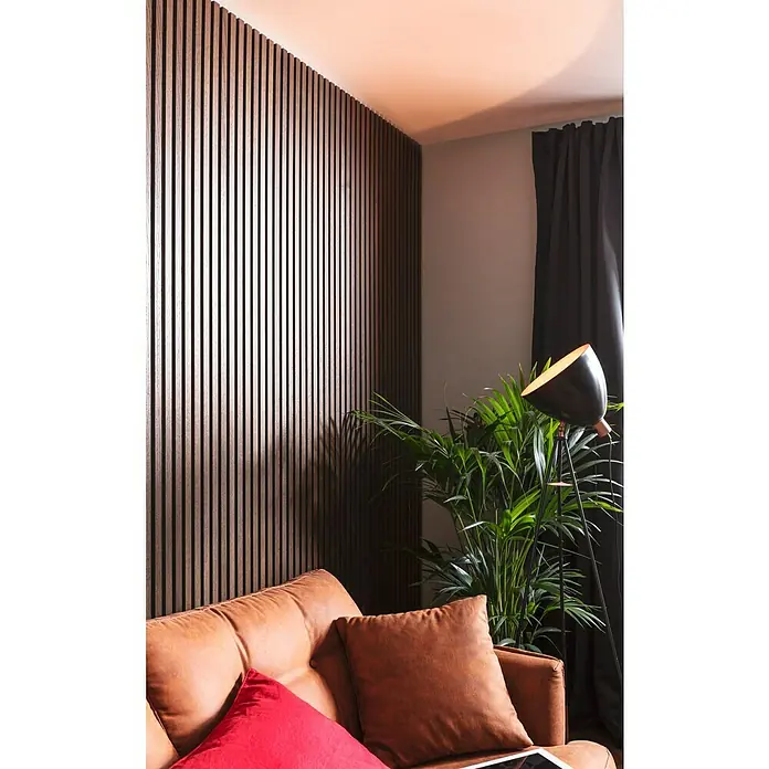 FibroTech Akustikpaneel Premium - Smoked Oak, 2.440 x 605 x 22 mm - Einrichtung mit Akustikpaneelen an der Wand, einem Ledersofa mit Kissen, einer Zimmerpflanze und einer Stehlampe, die eine gemütliche Atmosphäre schaffen.