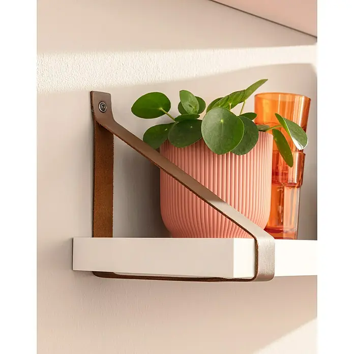 Dolle Soporte de estantería Loop - 2 ud., Piel, Carga límite balda: 12 kg - Primer plano de una estantería blanca con soporte de correa de cuero, con una planta de interior y vasos naranjas.