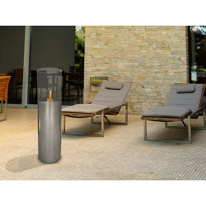 Purline Chimenea de bioetanol Iltia - 26 x 26 x 91 cm, Gris - Elegante escena al aire libre con un elegante calentador de patio, creando un ambiente cálido junto a las tumbonas.