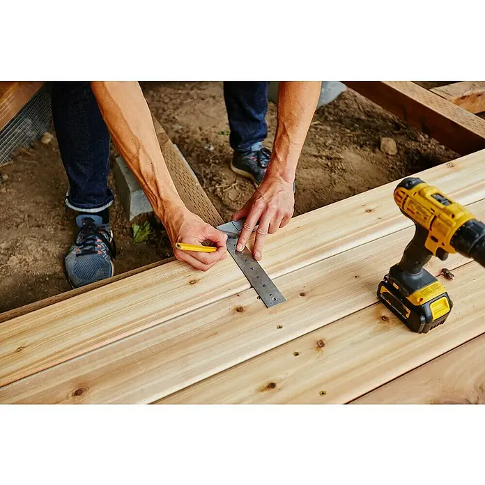 Holzschraube - Ø x L: 4,5 x 60 mm - Nahaufnahme eines Handwerkers, der mit einem Winkel und Bleistift Maße auf Holzbretter überträgt, neben einem gelben Akkuschrauber.
