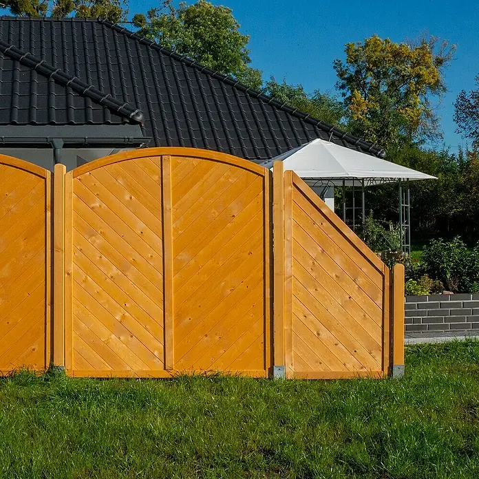 Sichtschutzelement Regensburg - 90 x 90/180 cm, Honig - Nahaufnahme eines neuen, hellbraunen Holzzauns, der ein Haus umgibt und Privatsphäre bietet, während die Sonne auf das frische Grün scheint.
