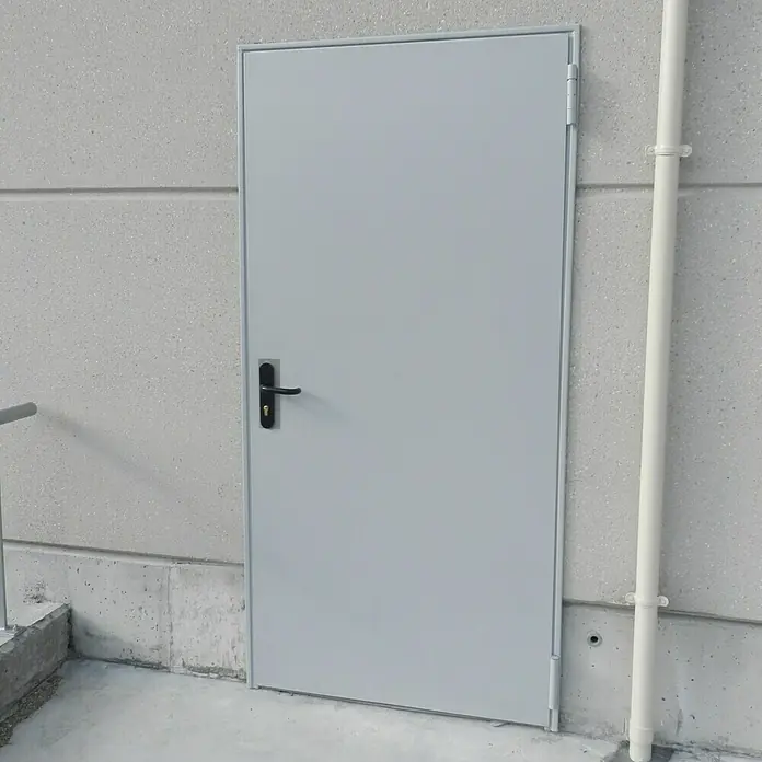Novoferm Puerta cortafuegos EI2 60 C5 - 88,5 x 203,5 cm, Izquierda, Blanco - Puerta metálica gris con manija negra en una pared de hormigón. Una puerta sencilla, pero robusta para aplicaciones industriales.