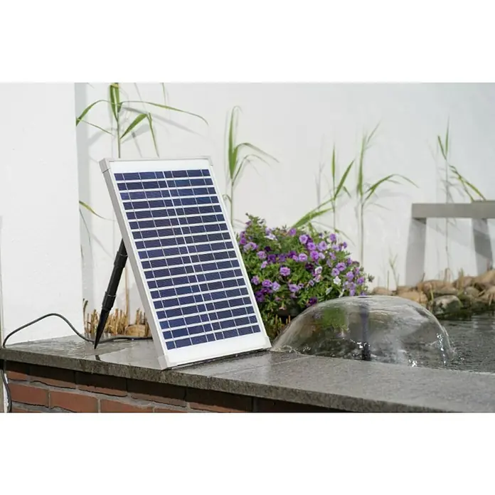 Ubbink Solar-Wasserspielpumpe Solarmax 1000 - Fördermenge pro Std.: 610 l - Solarpanel neben einem Brunnen, das umweltfreundliche Energie für den Betrieb liefert. Das Panel steht auf einer grauen Oberfläche mit Pflanzen im Hintergrund.
