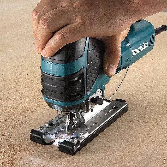 Makita Caladora eléctrica 4351FCTJ - 800 /min - 2.800 /min, Profundidad de corte máx. en madera: 135 mm, Número de niveles de elevación del péndulo: 4 ud. - Una sierra de calar Makita turquesa y negra es sostenida por una mano, cortando activamente una pieza de madera clara.