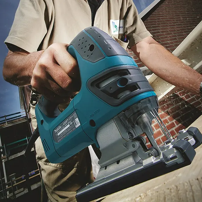 Makita Elektro-Pendelhubstichsäge 4350FCTJ - 800 /min - 2.800 /min, Max. Schnitttiefe in Holz: 135 mm, Anzahl Pendelhubstufen: 4 Stk. - Nahaufnahme einer blaugrünen Makita Stichsäge in Aktion, gehalten von einer Person, während sie Holz sägt.
