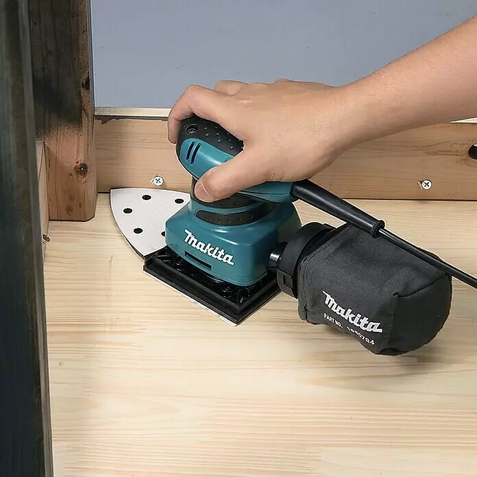 Makita Elektro-Schwingschleifer BO4565J - 200 W - Eine Hand benutzt einen türkis-schwarzen Makita Dreieckschleifer mit Staubbeutel zum Schleifen von hellem Holz.