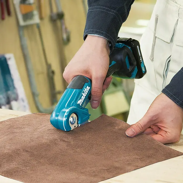 Makita CXT 12V max. Cortador universal de batería CP100DZ - 12 V, Sin batería, Profundidad máx. de corte: 6 mm - Un primer plano de un cortador textil inalámbrico Makita en acción, cortando un trozo de tela marrón. ¡Cortes de precisión facilitados!