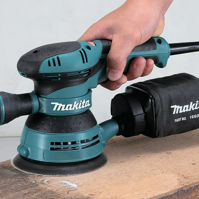 Makita Elektro-Exzenterschleifer BO5041J - 300 W, Durchmesser Schleifteller: 125 mm - Nahaufnahme eines Makita Exzenterschleifers, der auf einem Holzbrett verwendet wird. Das Elektrowerkzeug ist für feine Schleifarbeiten konzipiert.